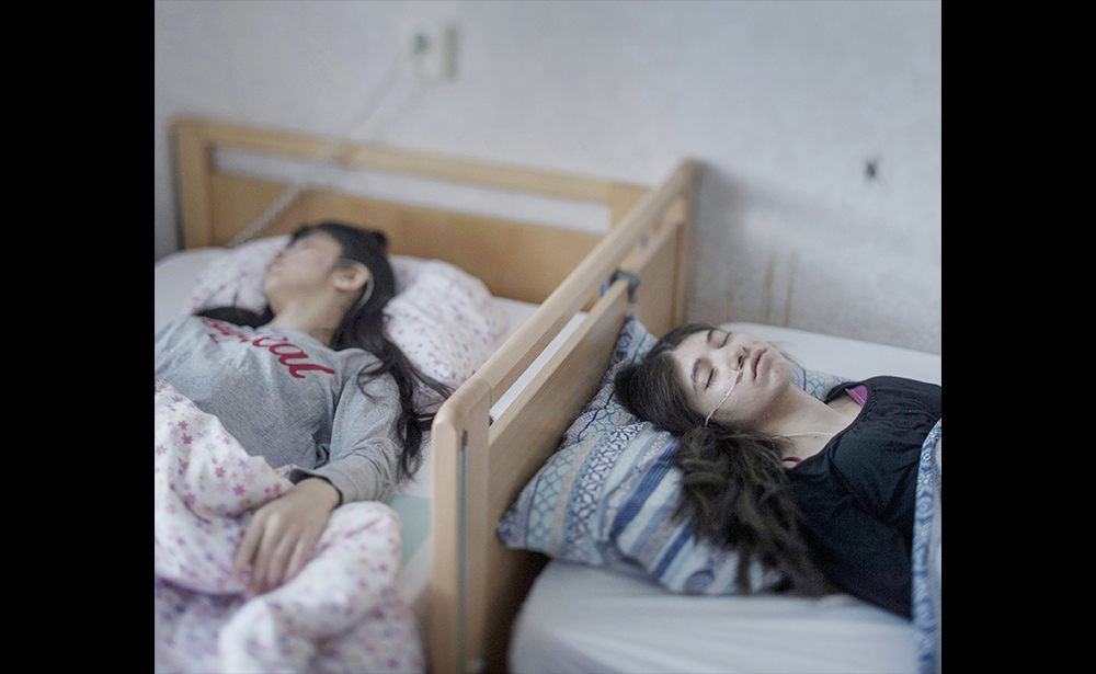 Giải nhất chủ đề Con người (hạng mục ảnh đơn) Magnus Wennman đã chụp bức ảnh này ở Horndal, Thụy Điển, quê hương của ông. Djeneta (phải) đã nằm liệt giường trong hai năm rưỡi trong khi em gái của cô, Ibadeta, nằm trên giường trong 6 tháng vì “hội chứng từ bỏ”. Theo lời giới thiệu trên website World Press Photo, hội chứng này khiến con người trở nên thụ động, không thể di chuyển, không thể trò chuyện, ăn uống, không phản ứng trước những kích thích vật lý. (Magnus Wennman)