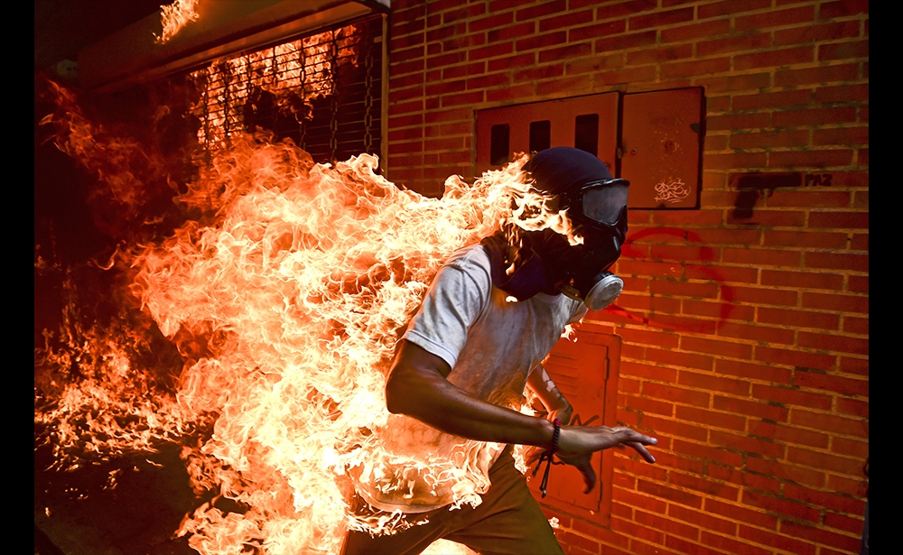 Ảnh của năm Cuộc thi ảnh báo chí danh giá và uy tín nhất thế giới đã công bố những bức ảnh chiến thắng được lựa chọn từ 73.000 bức ảnh của các phóng viên ảnh đến từ 125 quốc gia. Phóng viên ảnh Ronaldo Schemidt của hãng tin Pháp AFP đã giành được giải danh giá nhất Bức ảnh của năm - World Press Photo of the Year đồng thời xếp nhất ở hạng mục bắt khoảnh khắc - Spot News Singles. Bức ảnh chụp một người biểu tình đeo mặt nạ phòng độc, lưng bốc cháy trong cuộc đụng độ với cảnh sát chống vũ trang Venezuela ở thủ đô Caracas vào ngày 3 tháng 5 năm 2017. (Nguồn: Ronaldo Schemidt / AFP)