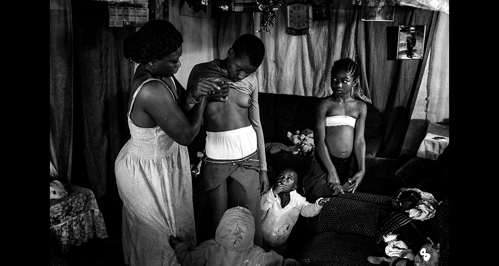 Giải nhất chủ đề đương đại, (hạng mục ảnh bộ) Nhiếp ảnh gia Ai Cập Heba Khamis đã chụp bộ ảnh Banned Beauty miêu tả truyền thống ép ngực ở Cameroon. Để tránh bị hãm hiếp và mang thai quá sớm, các thiếu nữ cố gắng hạn chế sự phát triển của ngực bằng nhiều cách khác nhau. Trong ảnh là Veronica, 28 tuổi, đang xoa bóp ngực cho cô con gái 10 tuổi Michelle ở Bafoussam, Cameroon ngày 11-7-2016. Xoa ngực là cách làm truyền thống của người Cameroon. (Ảnh: Heba Khamis)