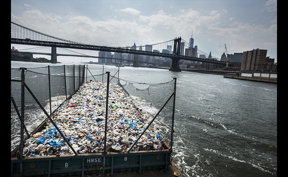 Giải nhất chủ đề Môi trường, (hạng mục ảnh bộ) Nhà báo ảnh người Hà Lan Kadir van Lohuizen của hãng ảnh Noor Images giành chiến thắng cho loạt ảnh Wasteland kể câu chuyện về việc xử lý rác thải tích tụ tại 6 thành phố lớn trên thế giới. Trong ảnh, một chiếc xà lan chứa hơn 300 tấn nhựa rời khỏi Bronx để chở đến một nhà máy tái chế ở Brooklyn, New York, ngày 26 tháng 5 năm 2016. (Ảnh: Kadir van Lohuizen / Hình ảnh NOOR)