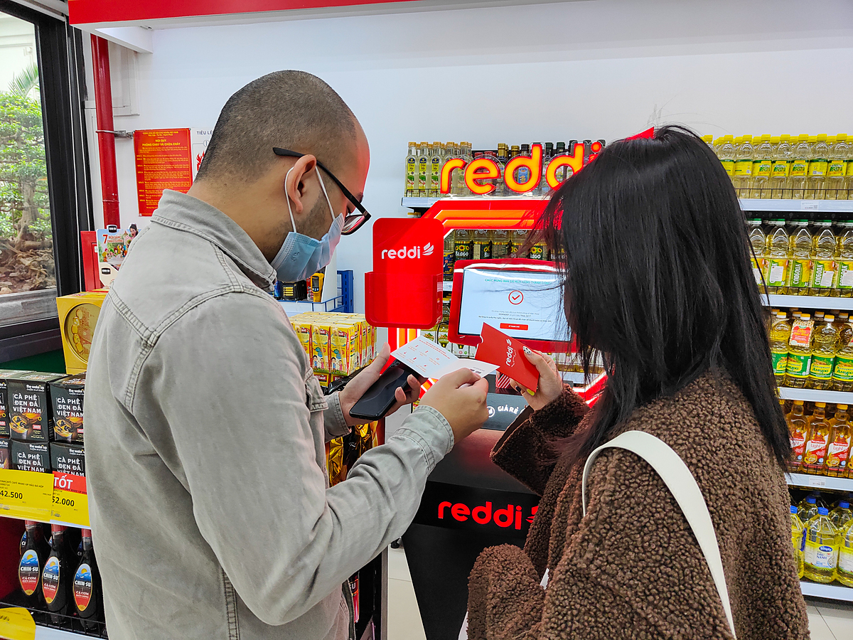 Nhân viên VinMart giới thiệu và hướng dẫn khách hàng hòa mạng Reddi. Reddi là mạng di động mới với ưu điểm sóng khỏe, tốc độ 3G nhanh và ổn định. Các gói cước đa dạng chỉ từ 99.000đ/tháng, sử dụng data không giới hạn. Reddi và kiosk Phúc Long thu hút phần lớn các khách hàng trẻ tuổi.