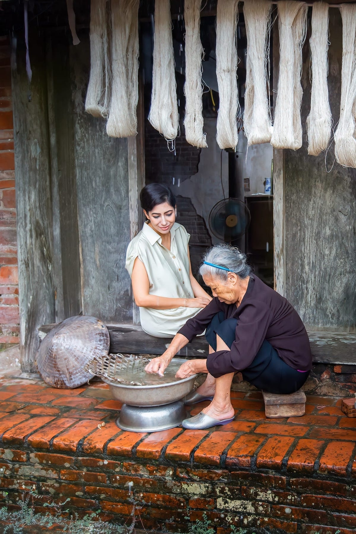 Công đoạn kéo sợi đũi tơ tằm, tức người thợ sẽ cho kén sau khi húi vào một chậu nước rồi dùng tay vê thành những sợi đũi tơ tằm thô.