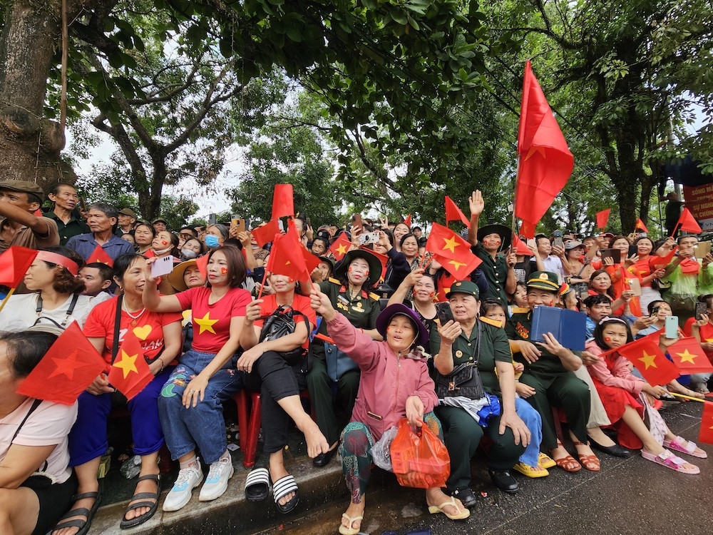 Người dân cầm cờ ngồi chờ khắp các ngả đường TP Điện Biên Phủ chờ đoàn diễu binh, diễu hành đi qua.