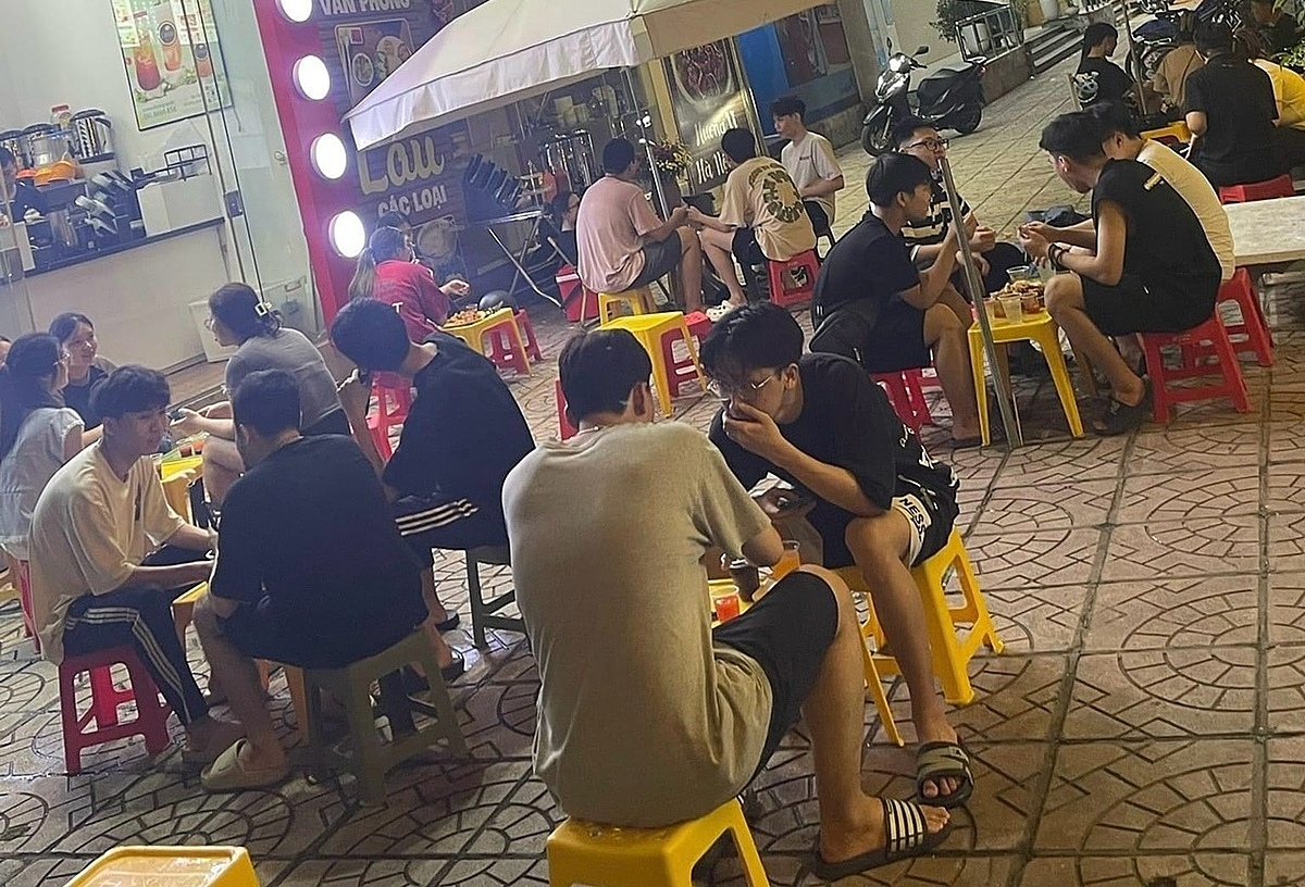 Khách hàng trẻ ngồi trên vỉa hè, bên một quán ăn đường phố ở Hà Nội.